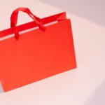 Vibrant orange paper shopping bag on a light pastel surface. Perfect for retail and branding visuals.