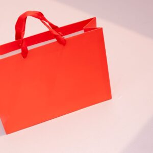 Vibrant orange paper shopping bag on a light pastel surface. Perfect for retail and branding visuals.
