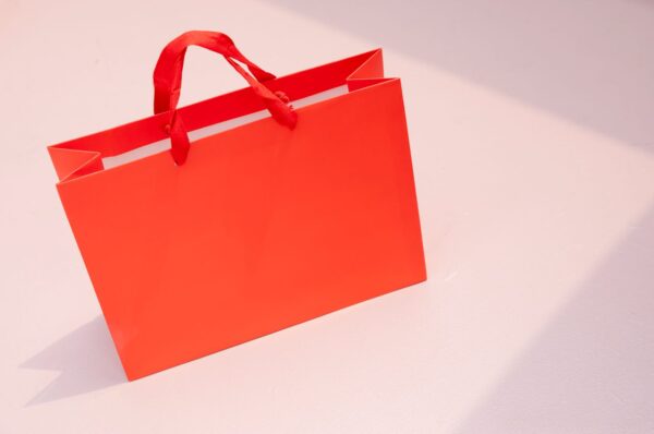 Vibrant orange paper shopping bag on a light pastel surface. Perfect for retail and branding visuals.
